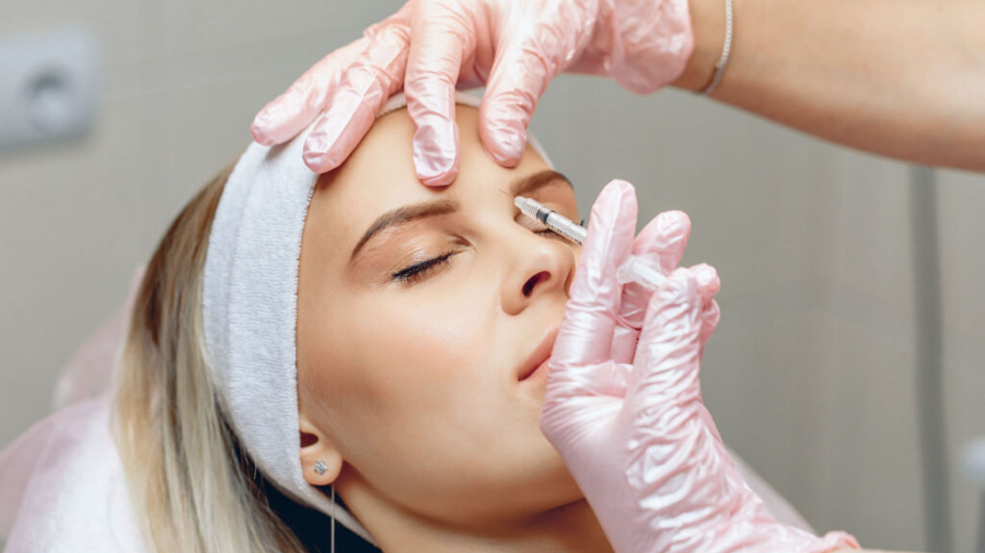 Neat master beautician who injects Botox in the brow area of a beautiful, charming patient. Anti-aging treatment concept